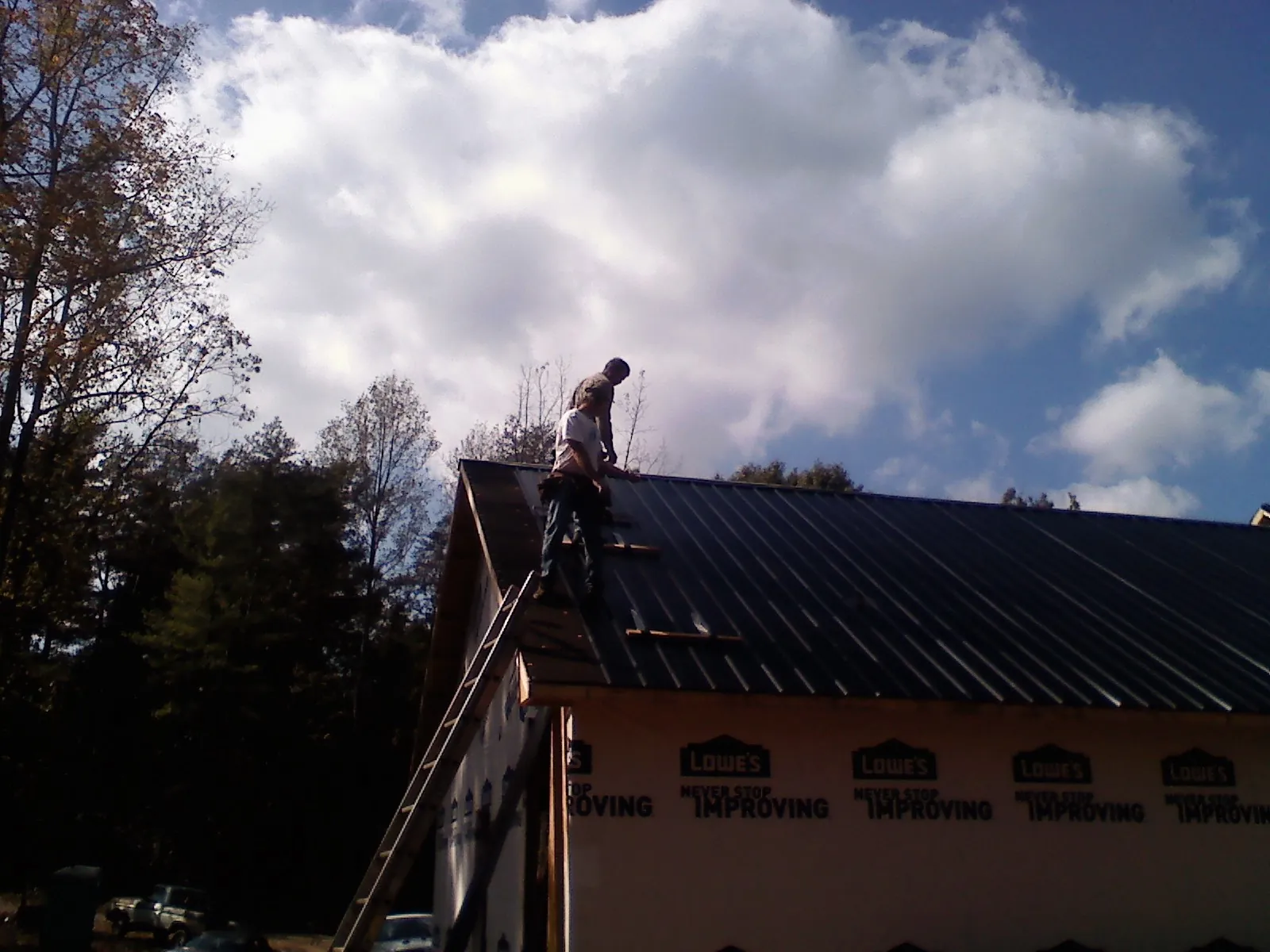 Roofer fastening dark metal panels high against a cloudy sky, from a Roof Inspection job in Mount Juliet