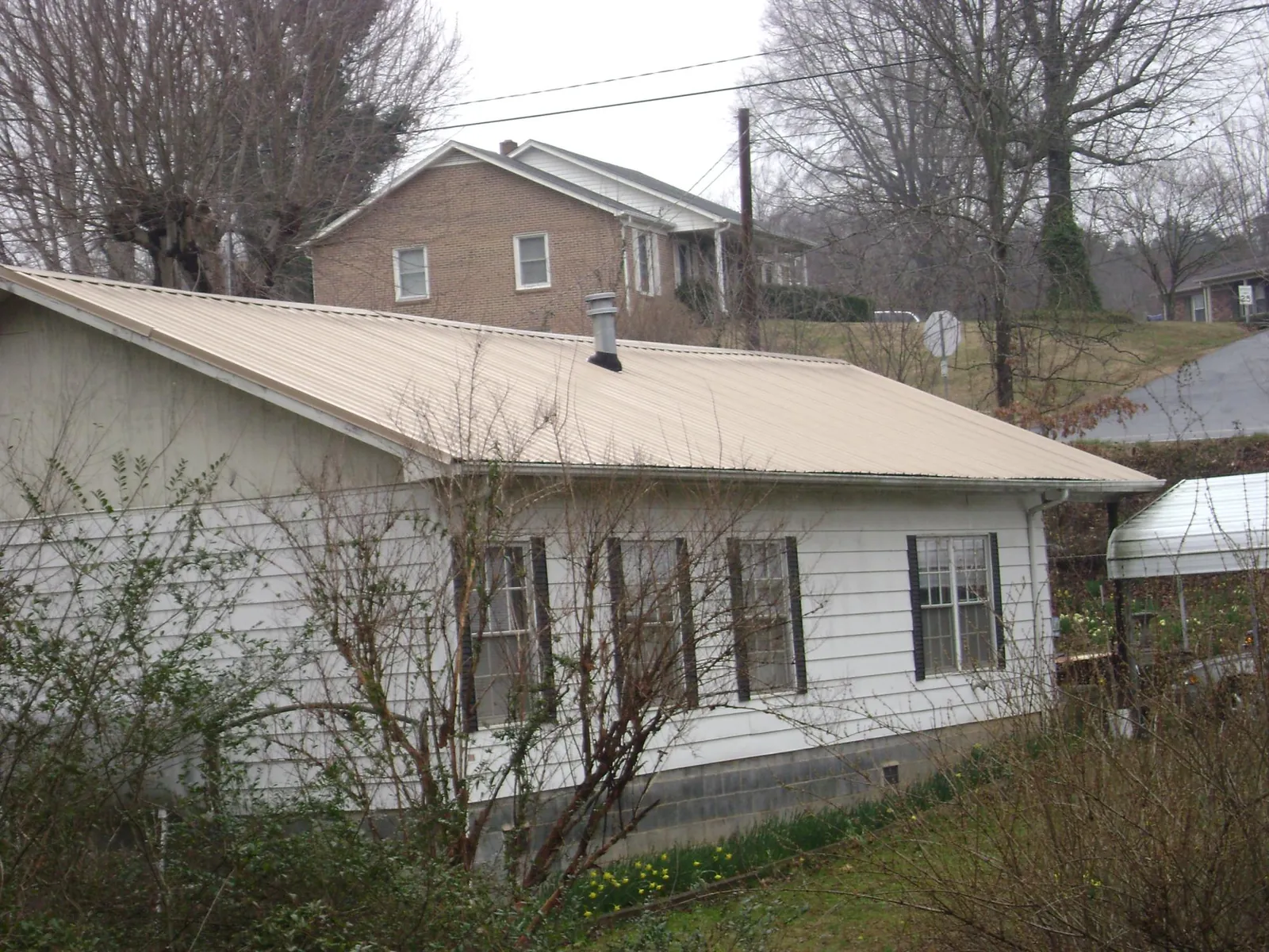 Tan metal roof on a white sided house set into a hillside — Commercial Roofing by Roofing Brothers in Mount Juliet